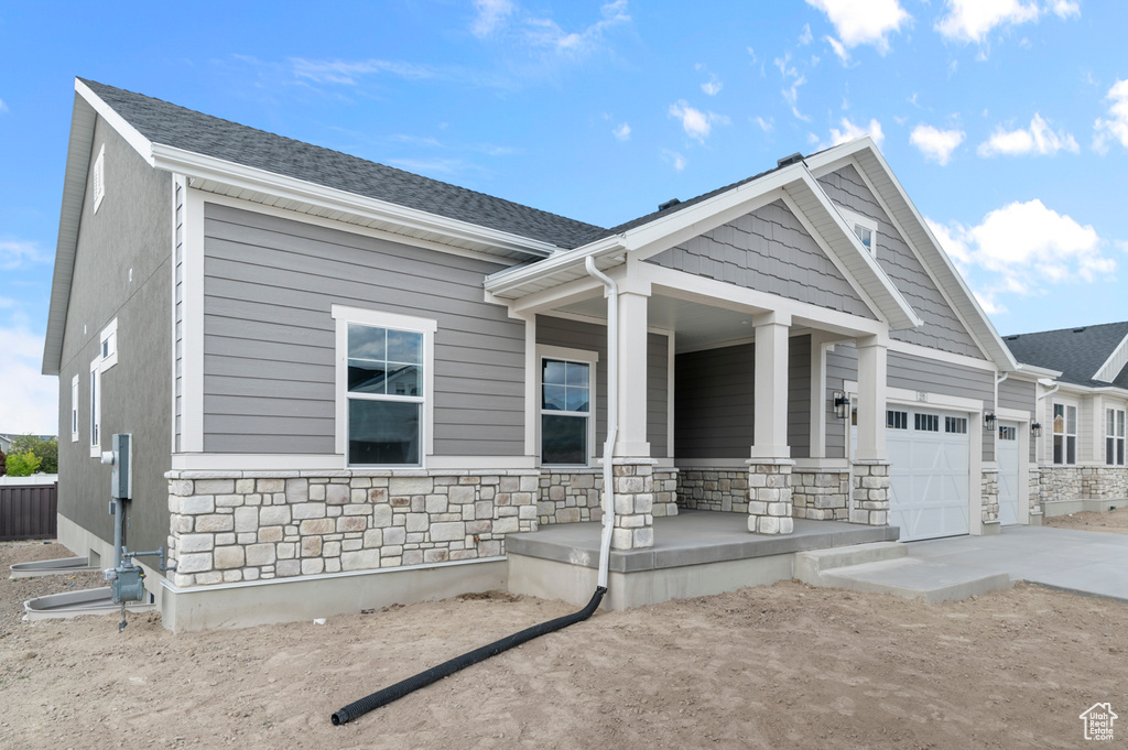Craftsman-style house featuring covered porch, stone siding, concrete driveway, and a garage