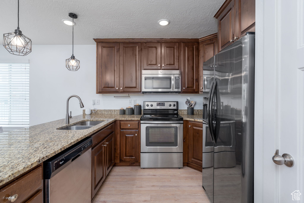 Kitchen featuring appliances with stainless steel finishes, light stone counters, a sink, light wood finished floors, and decorative light fixtures