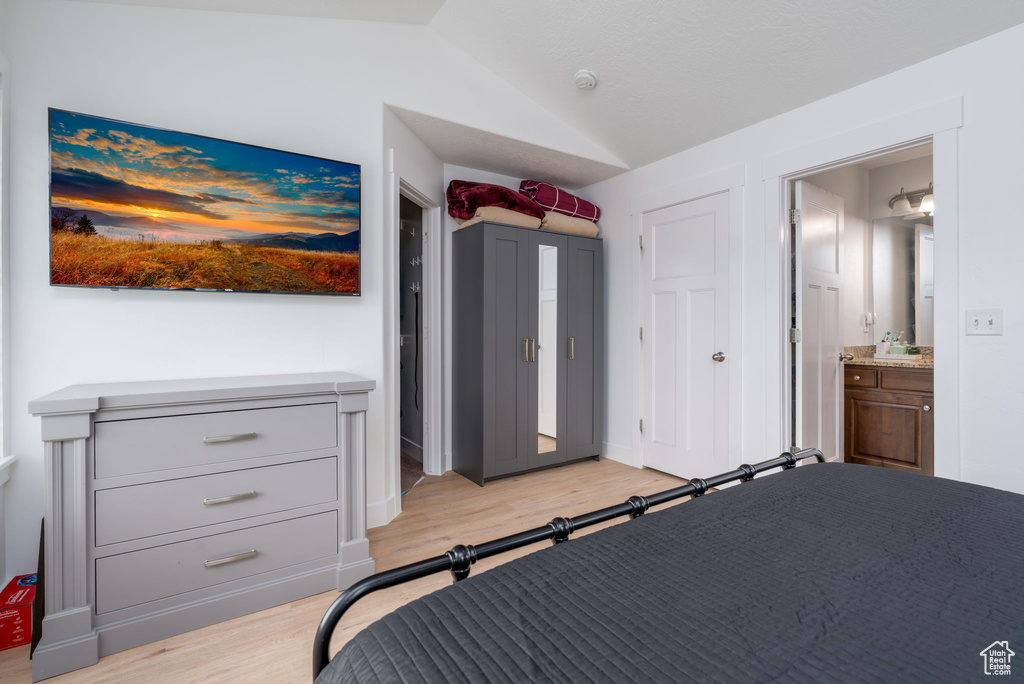 Bedroom featuring vaulted ceiling, light wood-type flooring, and ensuite bath