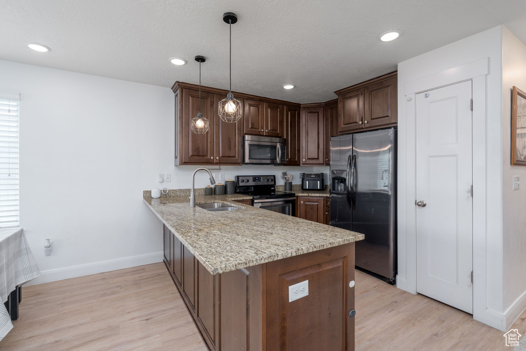 Kitchen featuring a sink, baseboards, a peninsula, stainless steel appliances, and light wood-style flooring