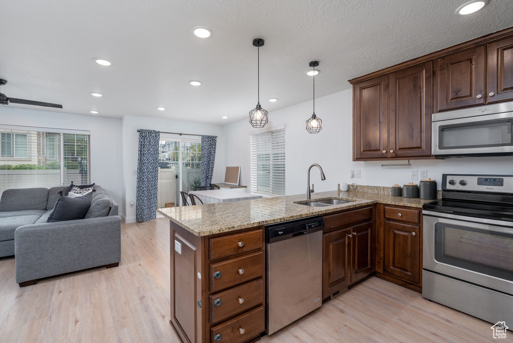 Kitchen with light wood-type flooring, a sink, a peninsula, open floor plan, and stainless steel appliances