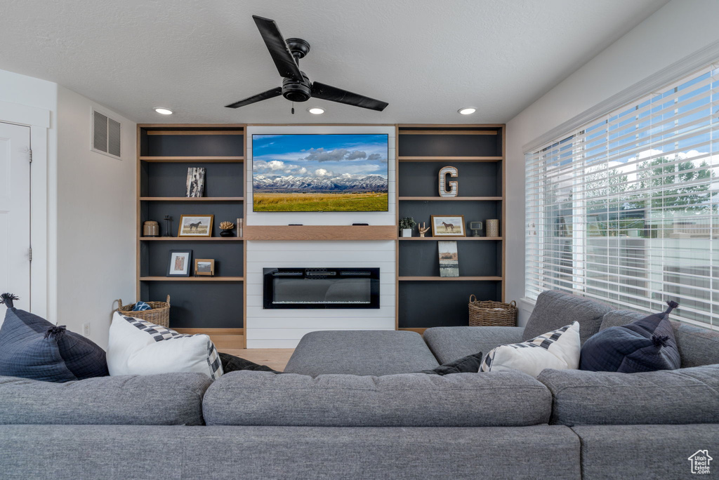 Living area featuring a ceiling fan, visible vents, built in features, a large fireplace, and recessed lighting