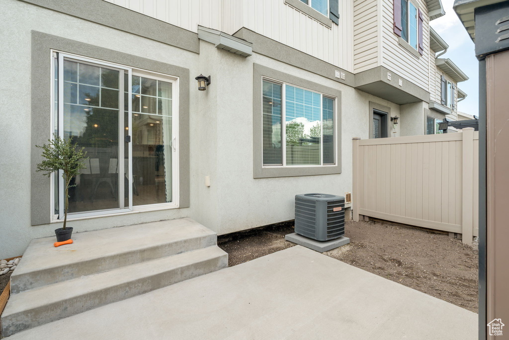 View of exterior entry featuring fence, central AC unit, a patio area, and stucco siding