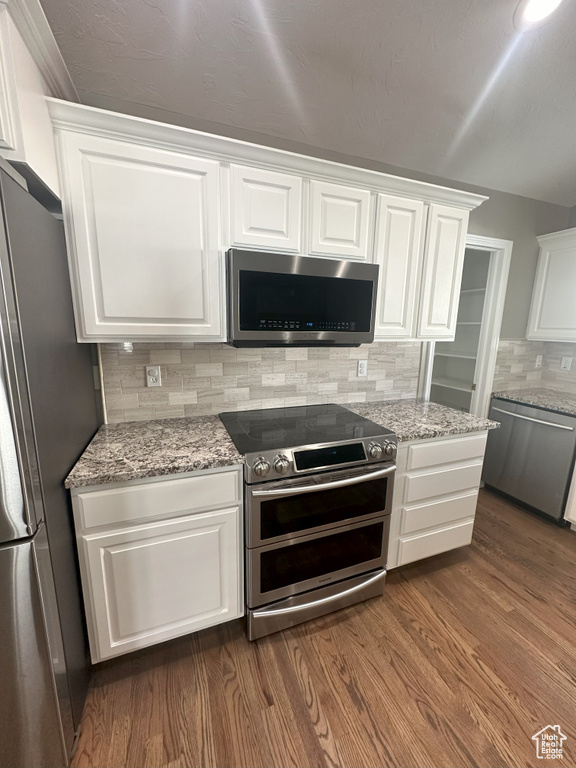 Kitchen with backsplash, appliances with stainless steel finishes, light stone countertops, dark wood-style floors, and white cabinetry
