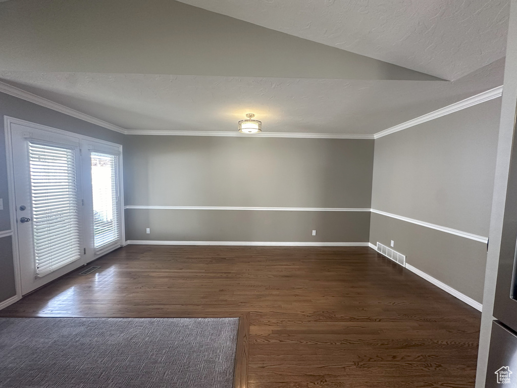 Empty room featuring visible vents, ornamental molding, wood finished floors, and lofted ceiling