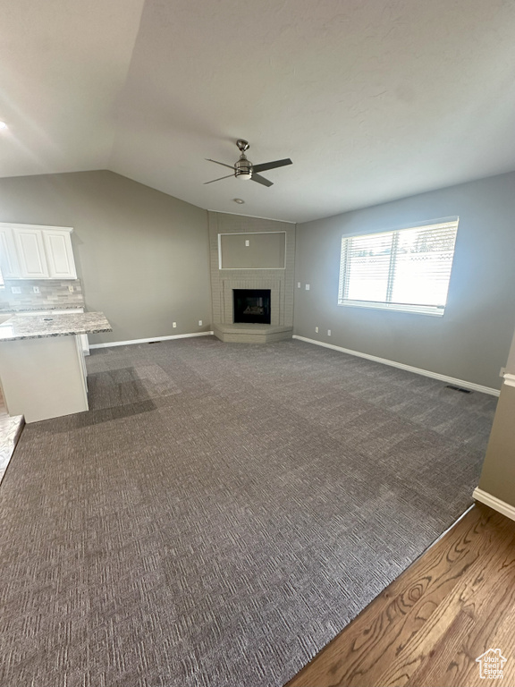 Unfurnished living room with a fireplace with raised hearth, a ceiling fan, baseboards, lofted ceiling, and visible vents
