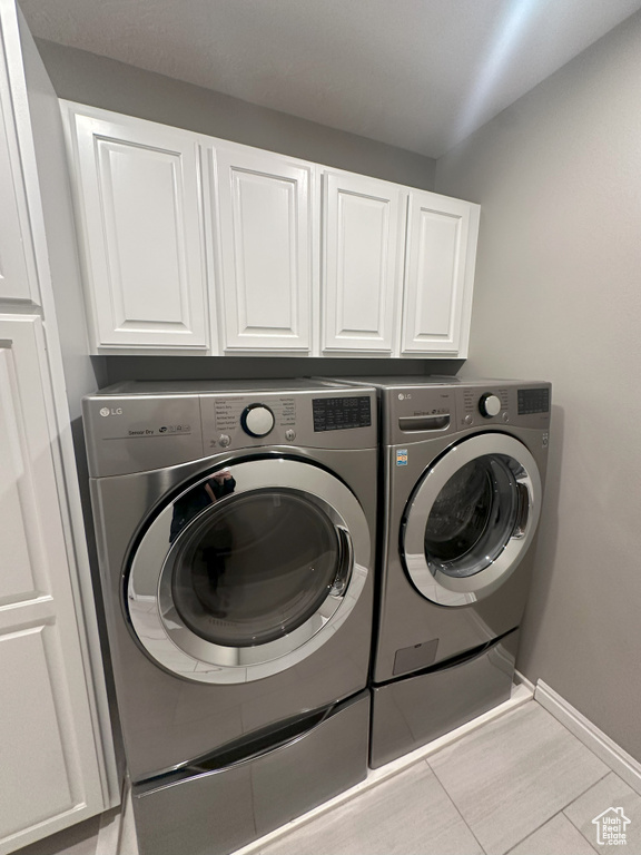 Laundry room featuring baseboards, cabinet space, tile patterned flooring, and washing machine and clothes dryer