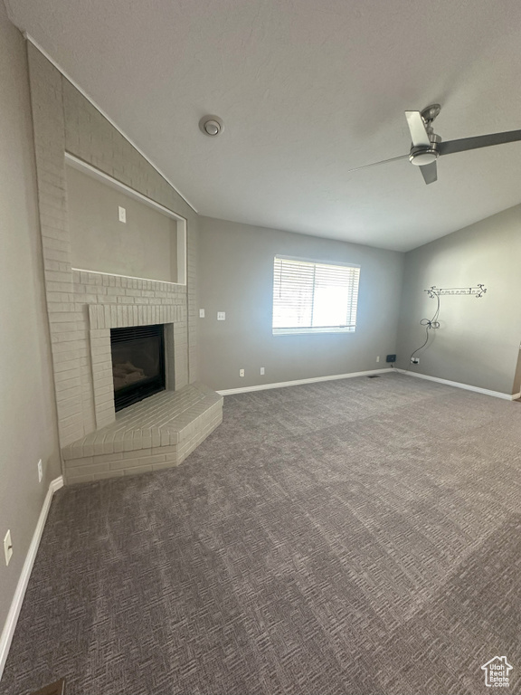Unfurnished living room featuring carpet flooring, a ceiling fan, baseboards, and a fireplace