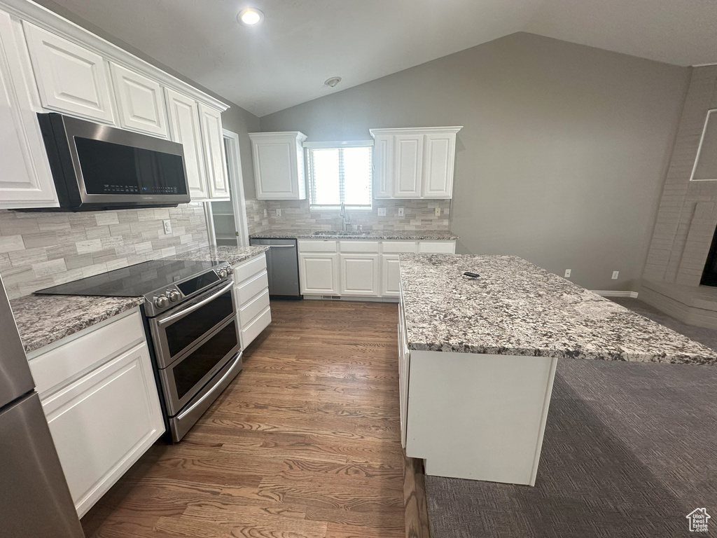 Kitchen featuring white cabinets, appliances with stainless steel finishes, a sink, lofted ceiling, and tasteful backsplash