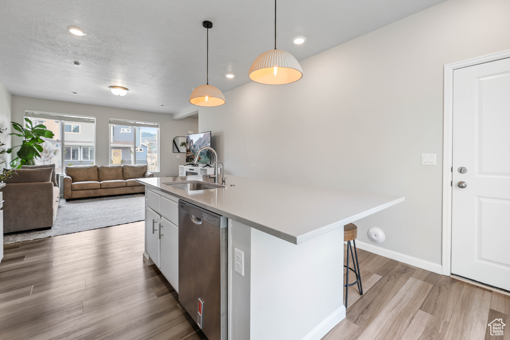 Kitchen featuring a center island with sink, a sink, light wood finished floors, dishwasher, and hanging light fixtures
