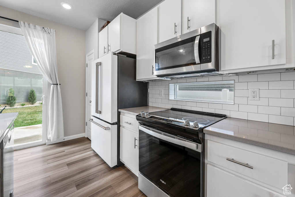 Kitchen with light wood-style floors, appliances with stainless steel finishes, backsplash, and white cabinetry