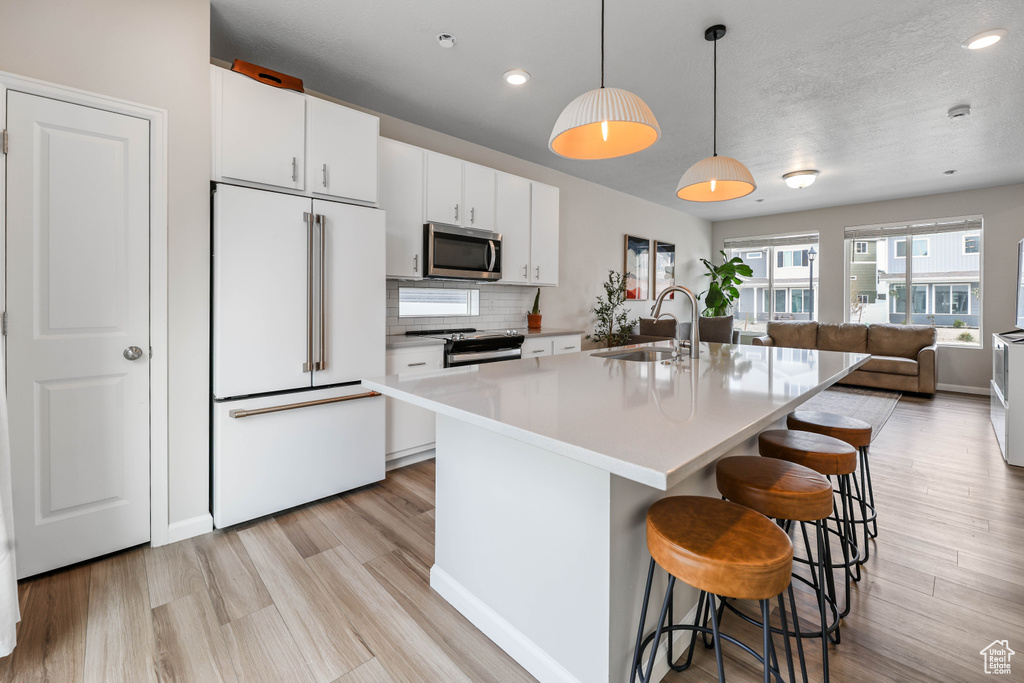 Kitchen with a breakfast bar area, white cabinetry, a sink, light wood-style flooring, and appliances with stainless steel finishes