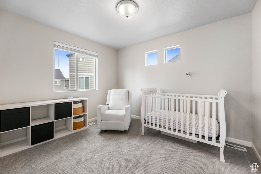 Carpeted bedroom with baseboards, visible vents, and a crib