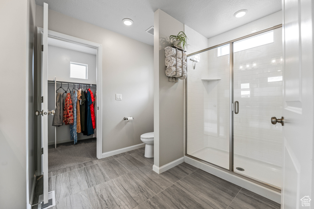 Full bath featuring baseboards, a walk in closet, a stall shower, and toilet