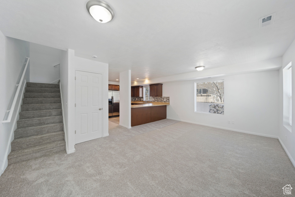 Unfurnished living room with baseboards, light carpet, and stairway