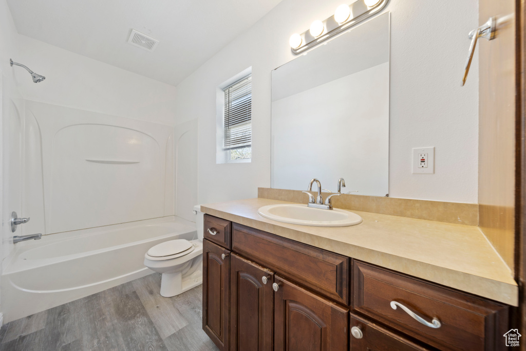 Bathroom with vanity, toilet, bathing tub / shower combination, wood finished floors, and visible vents