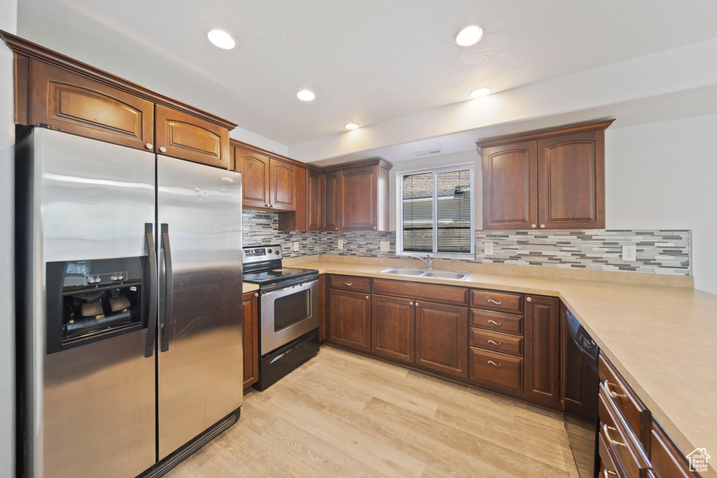 Kitchen with decorative backsplash, a sink, light countertops, light wood-style floors, and stainless steel appliances