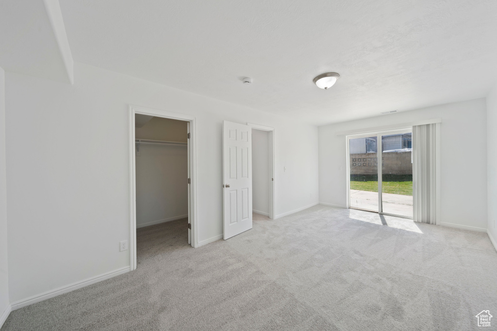 Unfurnished bedroom featuring baseboards, carpet, a walk in closet, and access to exterior