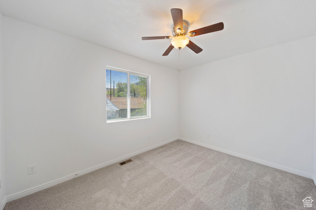 Empty room featuring baseboards, visible vents, light carpet, and ceiling fan