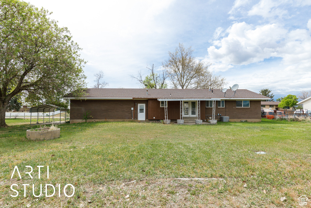 Rear view of property featuring a detached carport, fence, cooling unit, brick siding, and a lawn