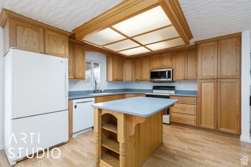 Kitchen featuring a sink, light wood-style floors, white appliances, brown cabinetry, and a center island
