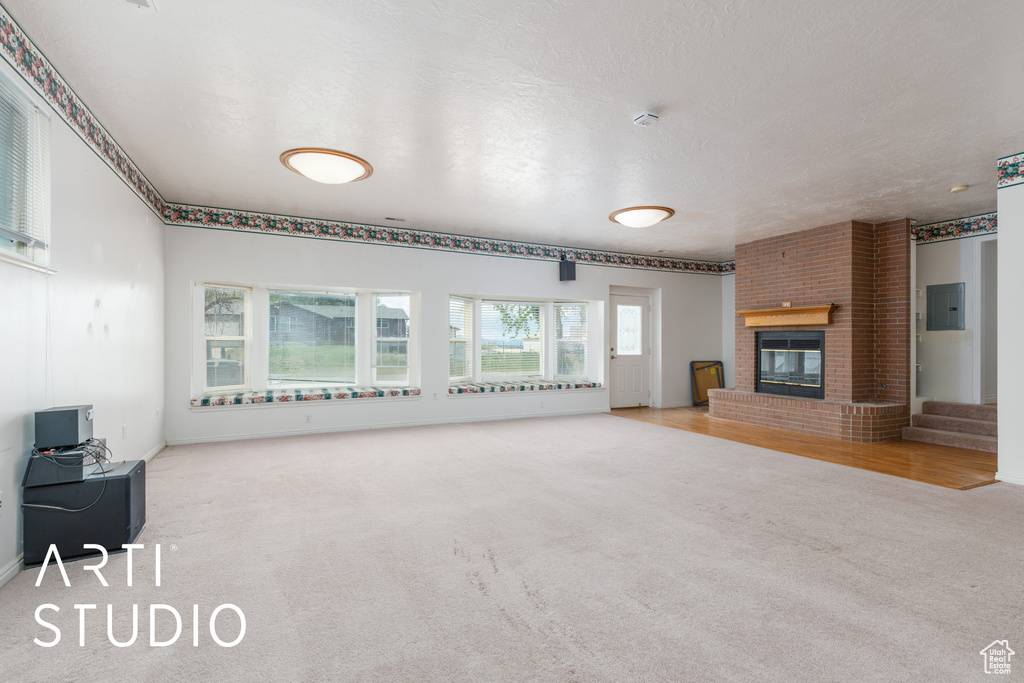 Unfurnished living room featuring baseboards, carpet, a brick fireplace, and electric panel
