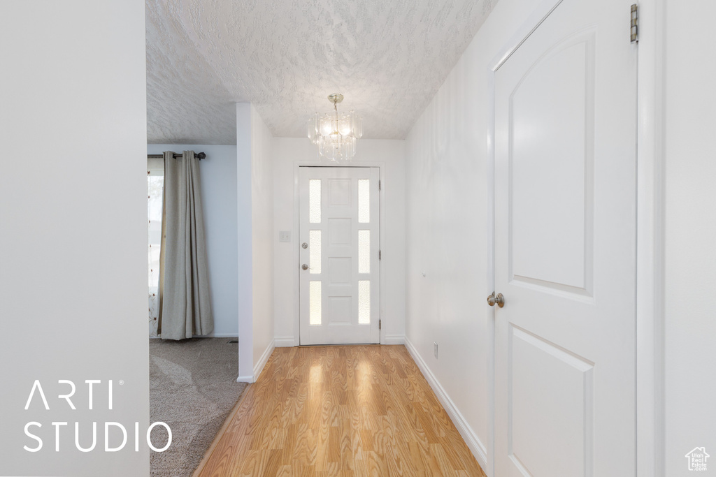 Foyer entrance with light wood-type flooring, a textured ceiling, a chandelier, and a wealth of natural light