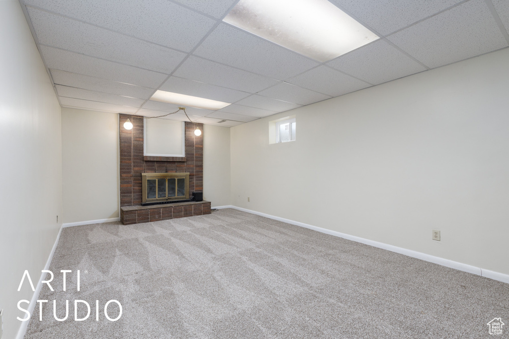 Unfurnished living room featuring baseboards, a drop ceiling, carpet flooring, and a brick fireplace