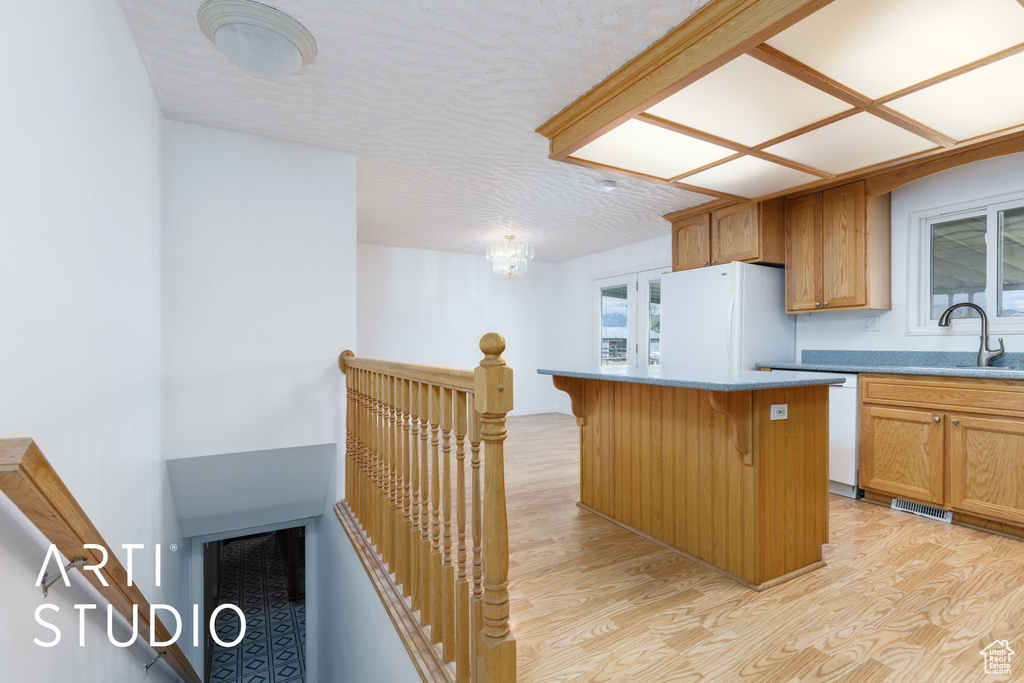 Kitchen featuring a kitchen island, a sink, freestanding refrigerator, a breakfast bar, and light wood-style flooring