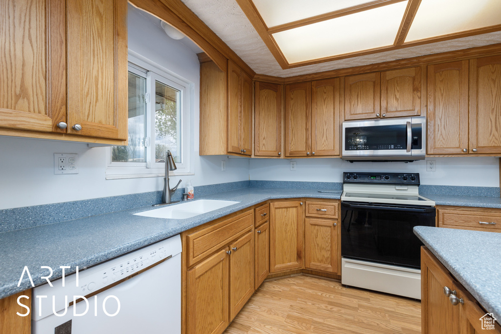 Kitchen with white dishwasher, a sink, light wood finished floors, electric range oven, and stainless steel microwave