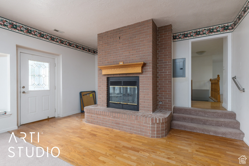 Unfurnished living room with a fireplace, baseboards, wood finished floors, and electric panel