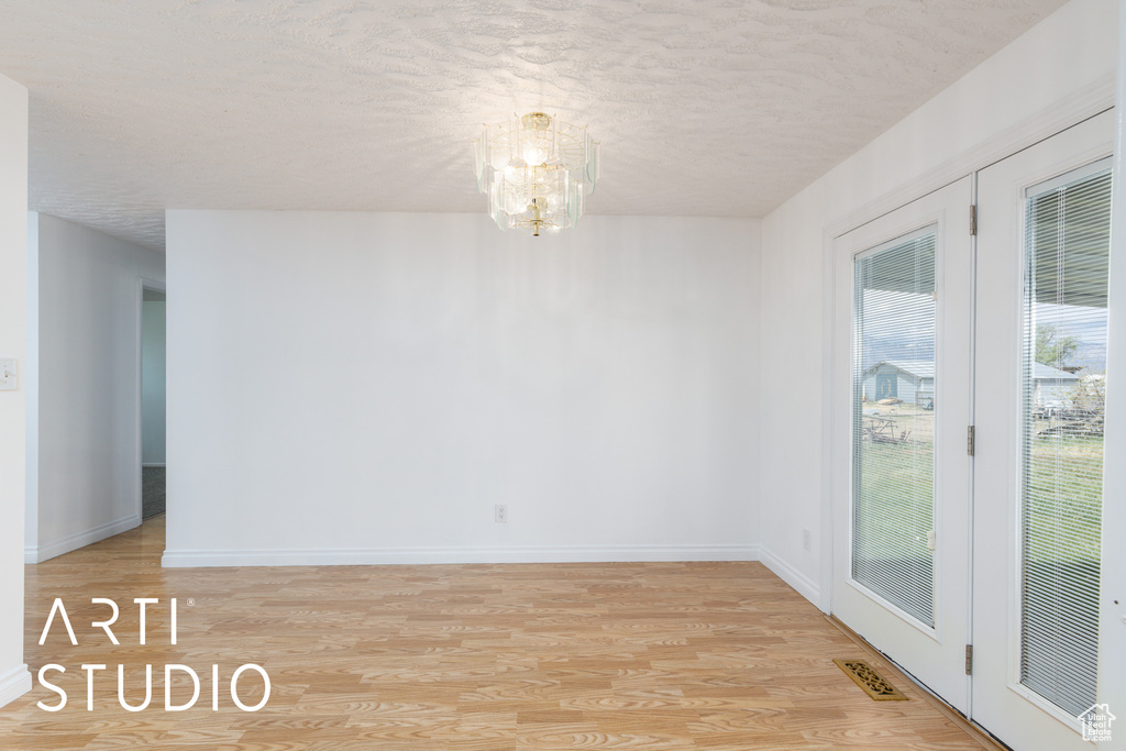 Unfurnished room with an inviting chandelier, visible vents, baseboards, a textured ceiling, and light wood finished floors