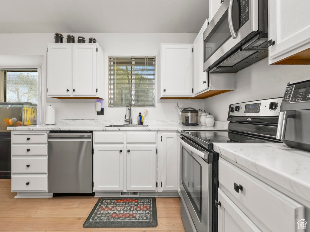 Kitchen with white cabinets, stainless steel appliances, a sink, and light wood-style flooring