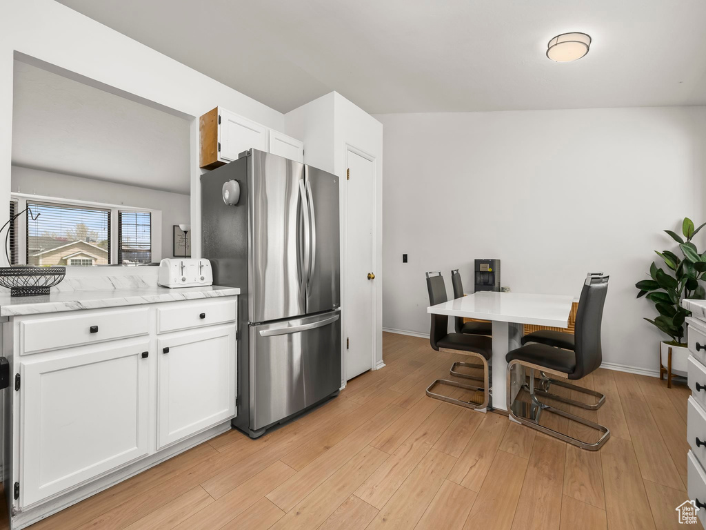 Kitchen featuring freestanding refrigerator, light stone countertops, baseboards, white cabinets, and light wood-style flooring