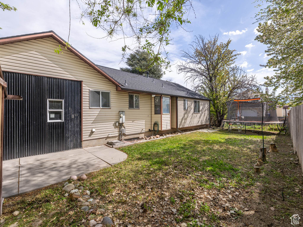 Rear view of property with a yard, a patio, fence, and a trampoline