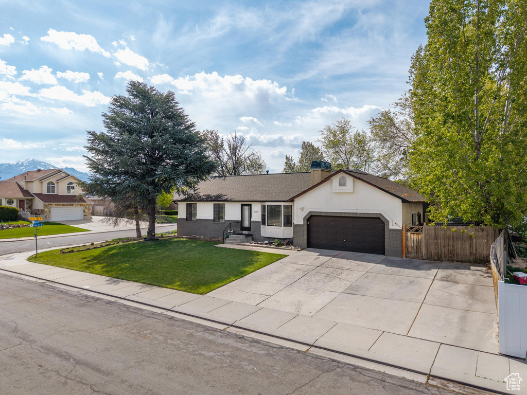 Ranch-style house with a garage, a front lawn, fence, stucco siding, and driveway