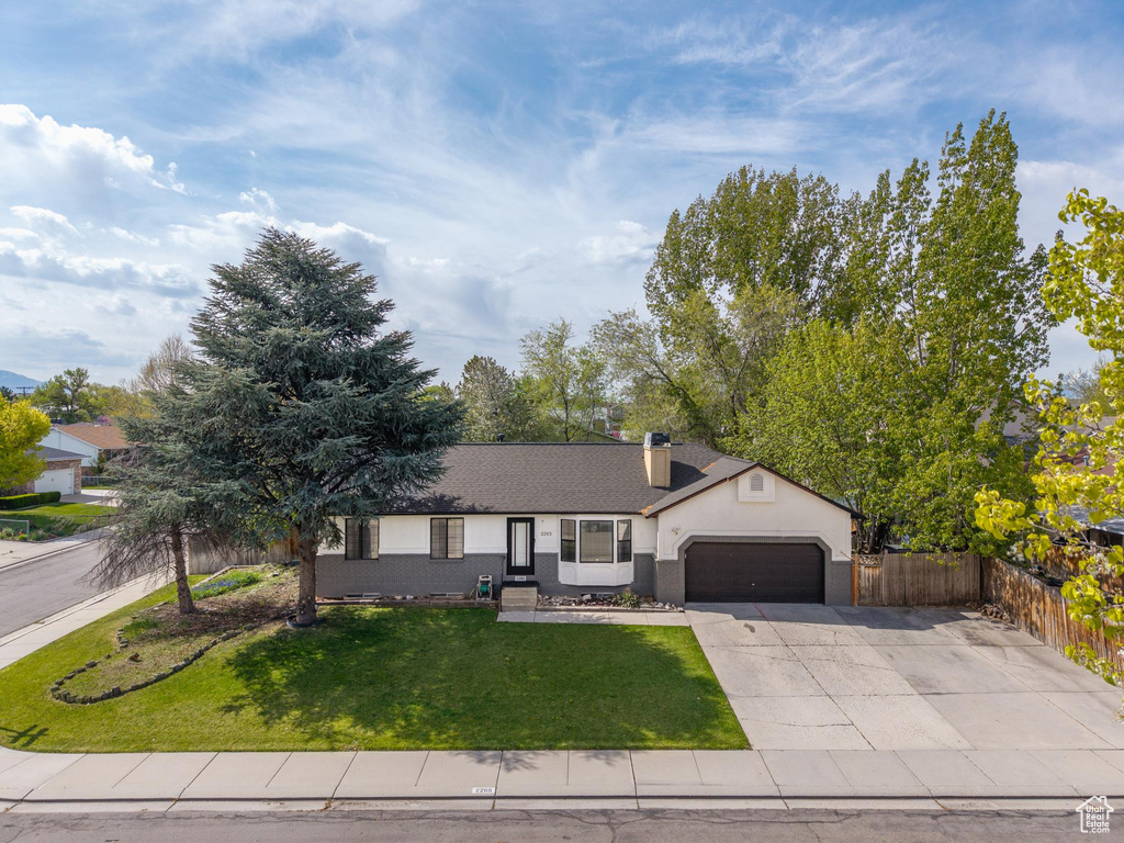 Ranch-style house with fence, an attached garage, a front lawn, a chimney, and driveway
