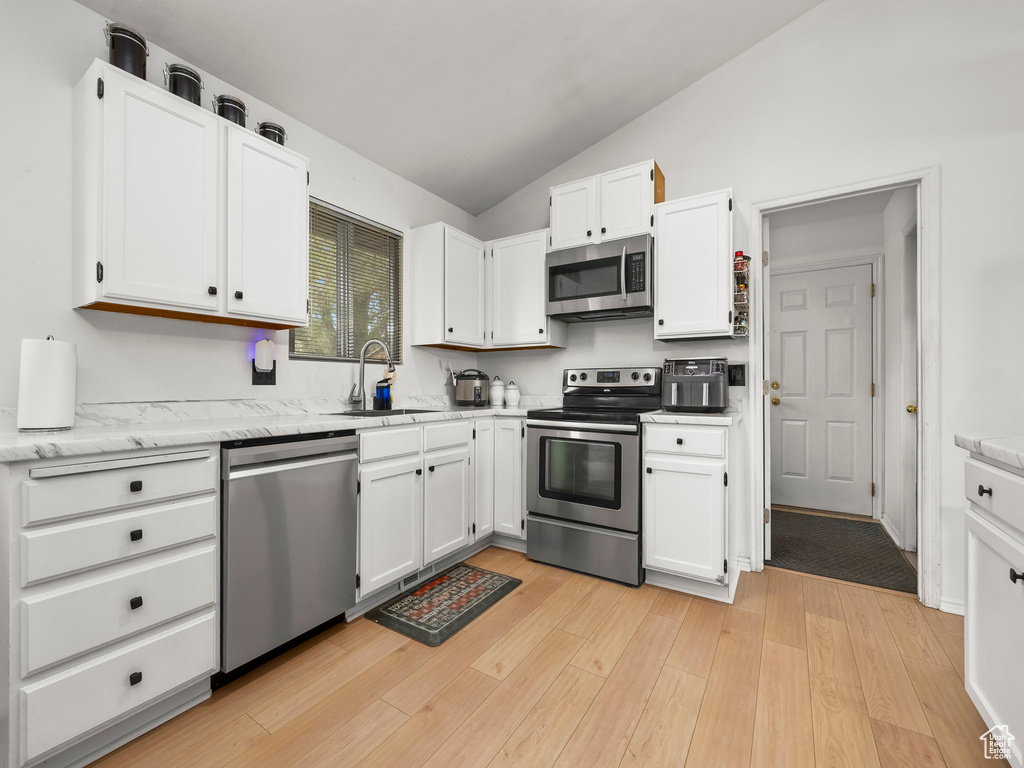 Kitchen featuring vaulted ceiling, a sink, light wood-style floors, stainless steel appliances, and white cabinetry