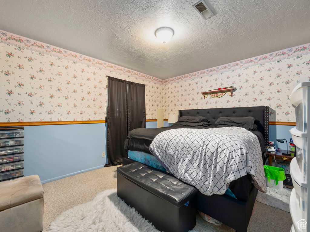 Bedroom featuring a textured ceiling, carpet, wallpapered walls, baseboards, and visible vents