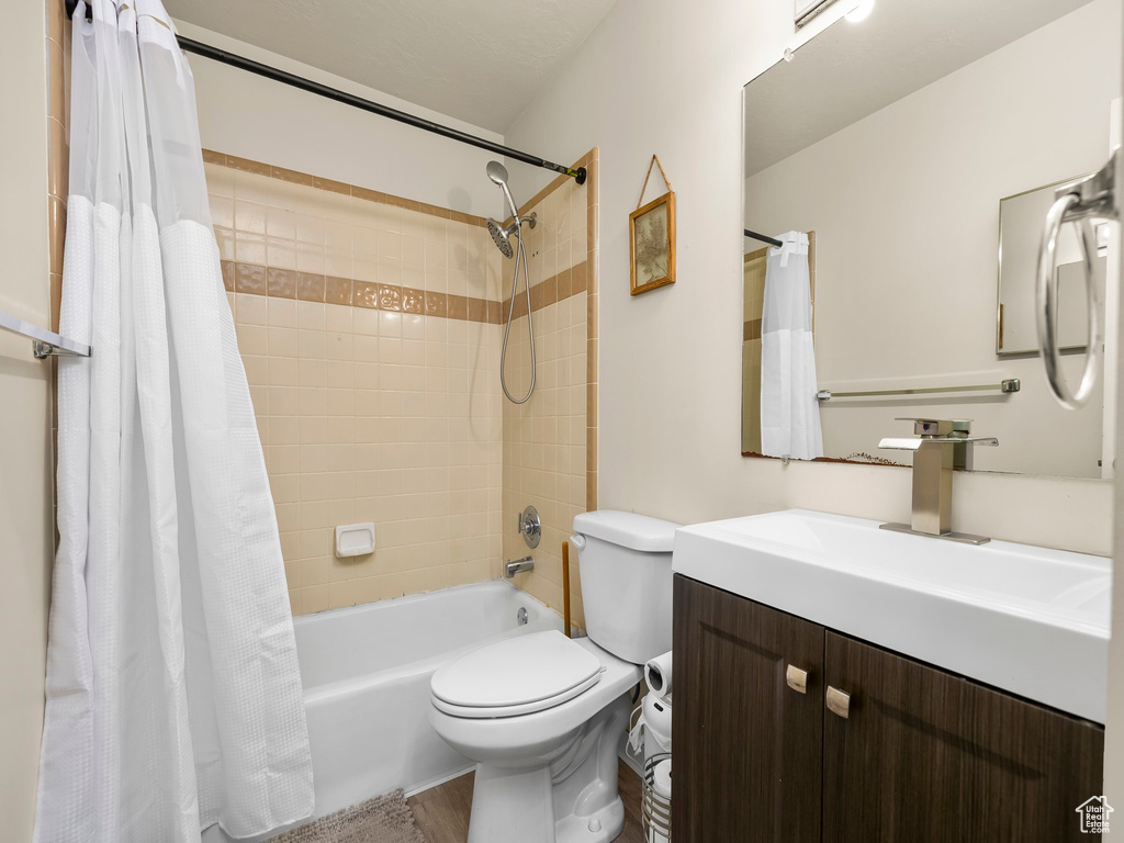 Bathroom featuring vanity, shower / tub combo with curtain, wood finished floors, and toilet
