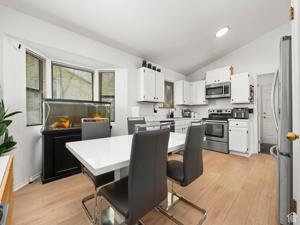 Kitchen with light countertops, white cabinetry, appliances with stainless steel finishes, and lofted ceiling