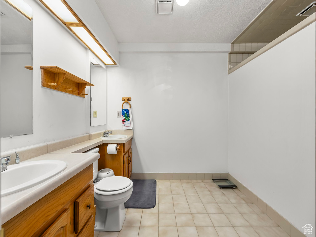 Full bath with toilet, tile patterned floors, two vanities, and a sink