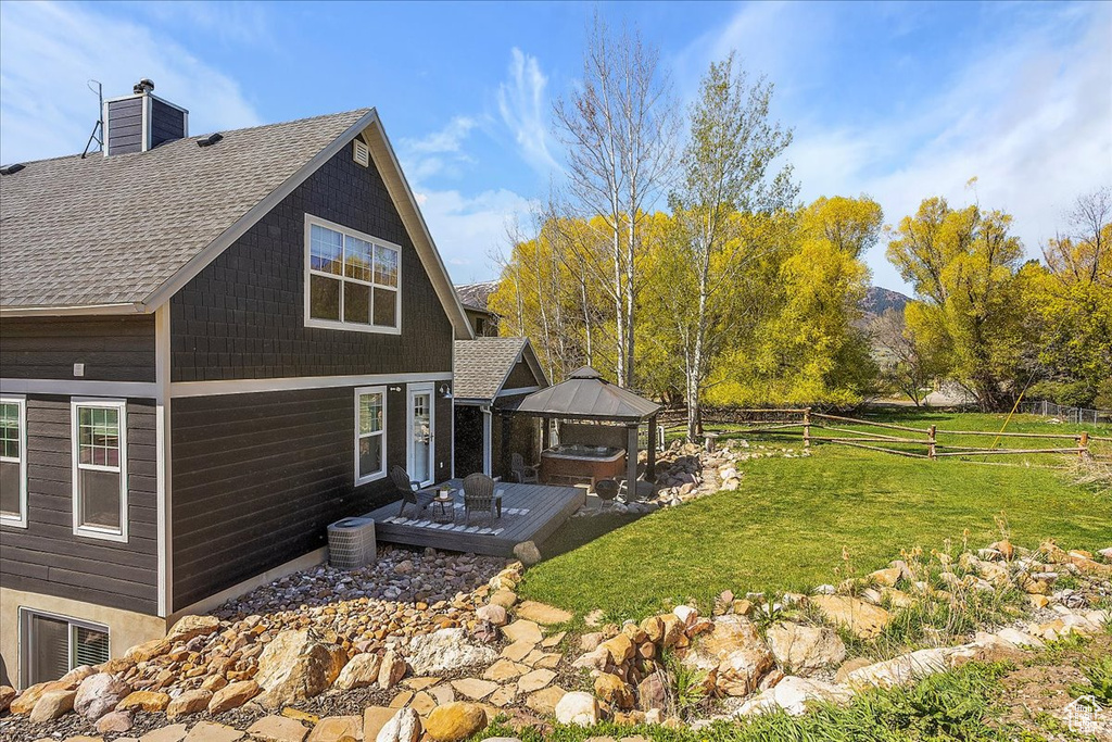 Exterior space with a lawn, fence, a shingled roof, a jacuzzi, and a gazebo
