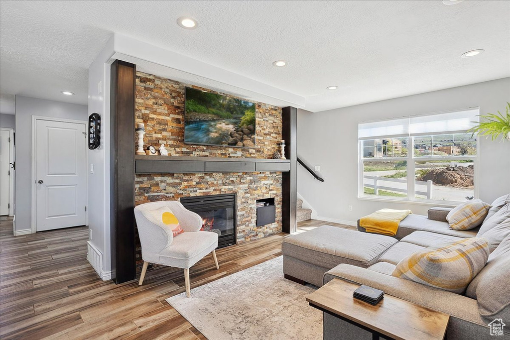 Living room featuring a textured ceiling, a stone fireplace, wood finished floors, baseboards, and recessed lighting