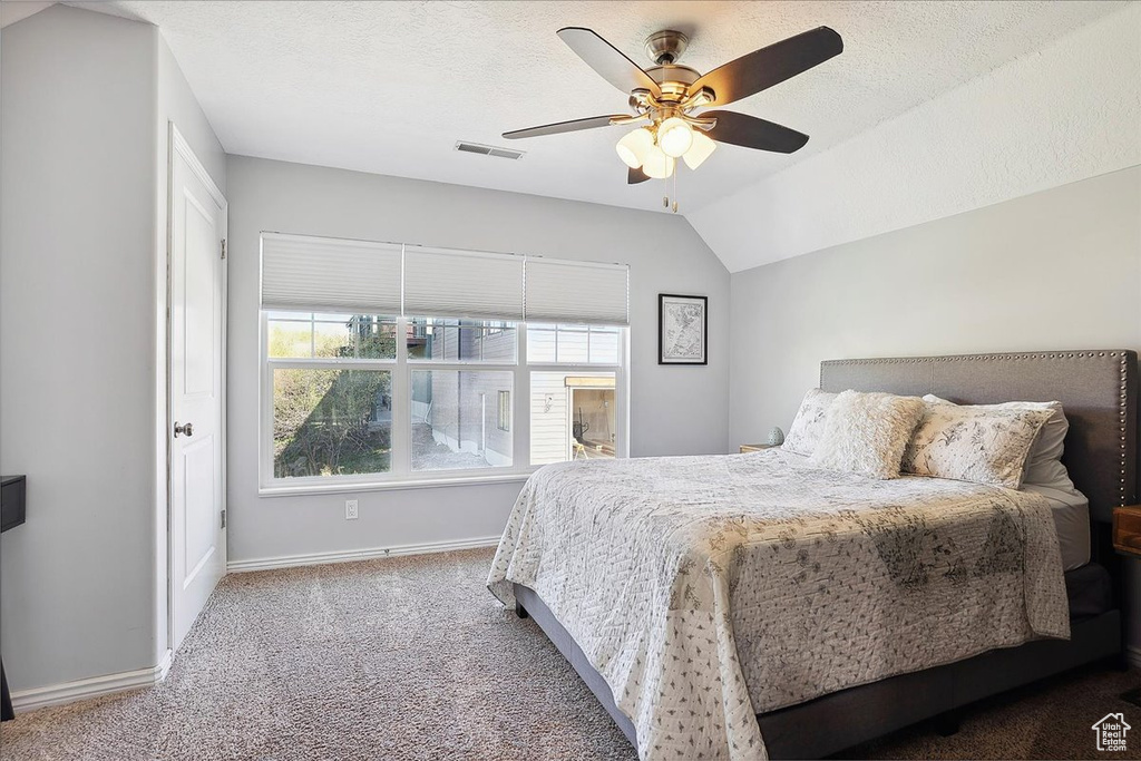 Carpeted bedroom with a ceiling fan, baseboards, visible vents, and vaulted ceiling