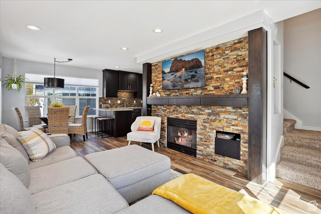 Living room featuring stairs, recessed lighting, a stone fireplace, and wood finished floors