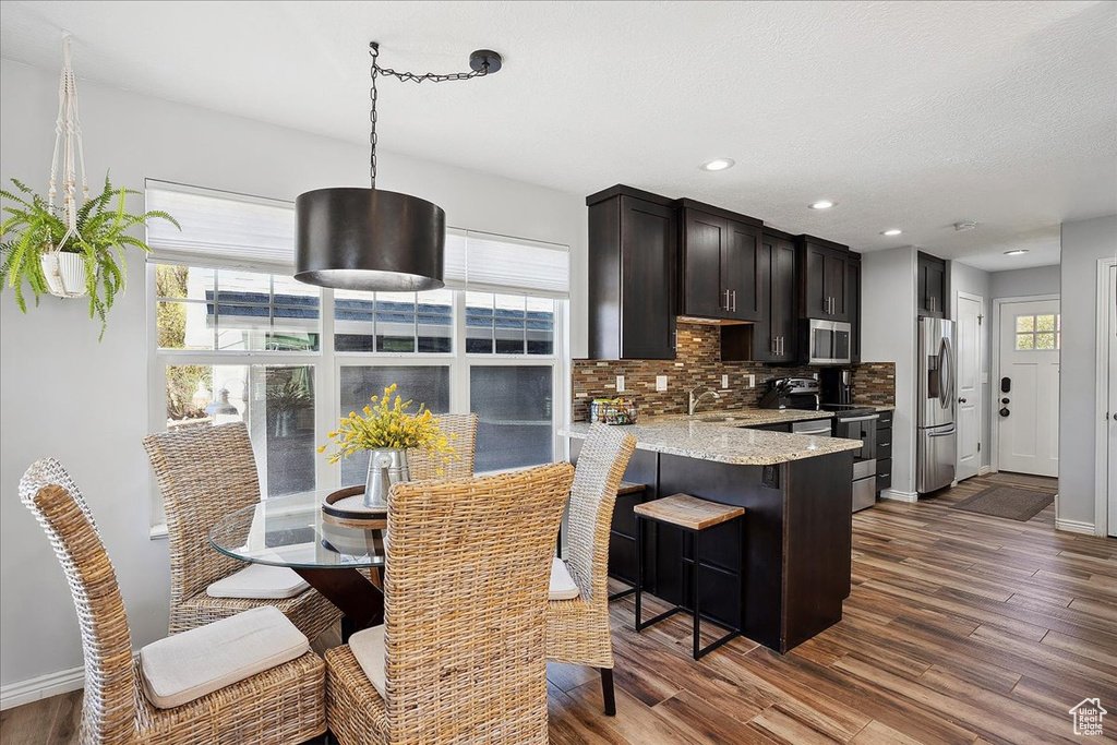 Kitchen with decorative backsplash, dark wood-style floors, light stone counters, a sink, and stainless steel appliances