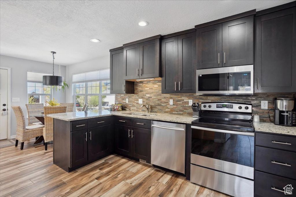 Kitchen featuring a peninsula, light stone counters, light wood finished floors, appliances with stainless steel finishes, and backsplash