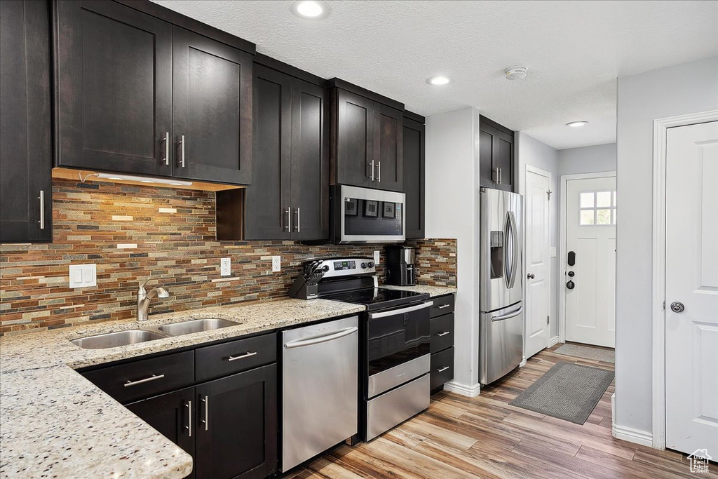 Kitchen with light stone countertops, a sink, light wood-style floors, stainless steel appliances, and tasteful backsplash