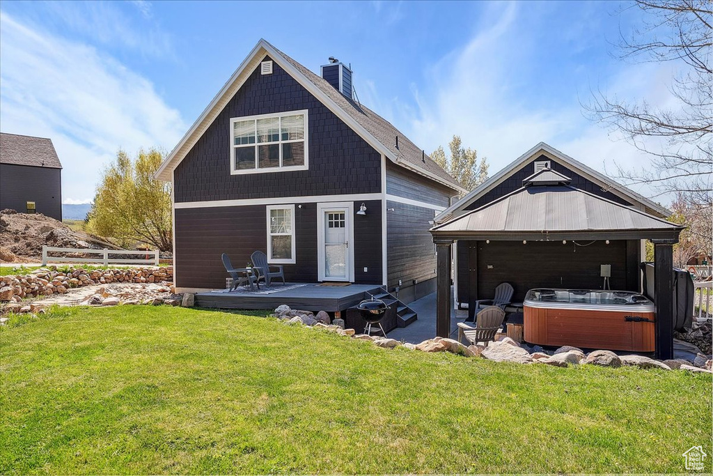 Rear view of property featuring a chimney, a lawn, a wooden deck, a hot tub, and a gazebo